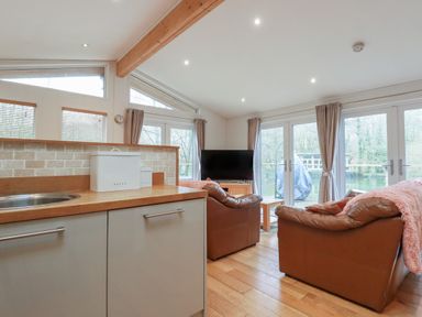 A kitchen area with cabinets and a sink adjoining a living room with leather sofas a television and large windows at 1 Miller's Island near Lanreath