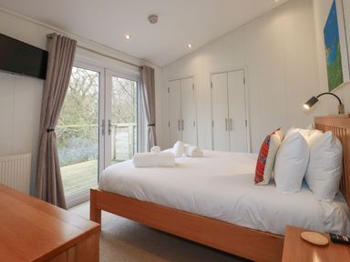 A bedroom with a bed with rolled towels pillows wood furniture glass doors and closets at 1 Millers Island near Lanreath
