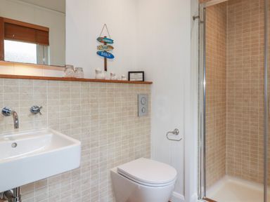 A bathroom with a sink to the left a toilet in the center and a shower with glass doors to the right at 1 Millers Island near Lanreath