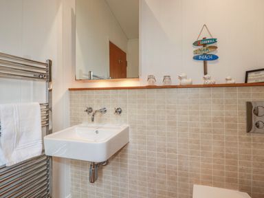 A bathroom with a wall-mounted sink a chrome towel rail with a white towel and decorative items on a shelf at 1 Millers Island near Lanreath