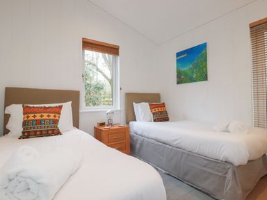 A bedroom with two single beds a wooden nightstand and windows with blinds at 1 Miller's Island near Lanreath