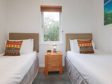 A bedroom with two single beds separated by a wooden nightstand with a lamp and clock at 1 Miller's Island near Lanreath