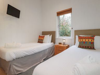 A bedroom with two single beds a wooden nightstand a lamp a window and a wall-mounted television at 1 Miller's Island near Lanreath