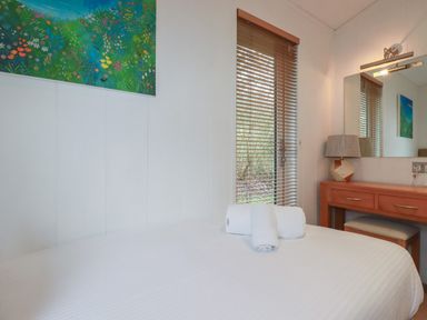 A bedroom with a bed, rolled towels, a window with blinds, a desk with a lamp, and a mirror at 1 Miller's Island near Lanreath