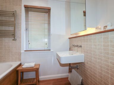 A bathroom with a wall-mounted sink wooden stool and a window with blinds at 1 Miller's Island near Lanreath