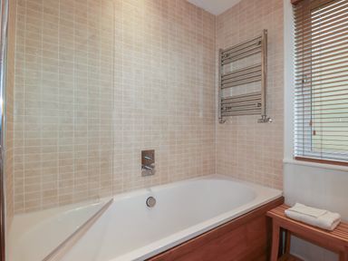 A bathroom with a bathtub a glass shower screen a towel rack and a wooden bench with a folded towel at 1 Miller's Island near Lanreath