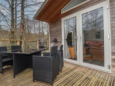 An outdoor wooden deck with black wicker chairs and a glass table at 1 Miller's Island near Lanreath