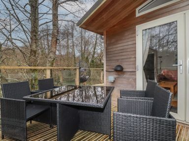 An outdoor deck with a black glass table and four black wicker chairs near wooden walls and glass doors at 1 Miller's Island near Lanreath