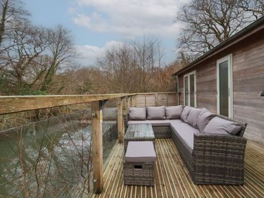 A wooden deck with outdoor wicker sofa and table overlooking a river at 1 Miller's Island near Lanreath