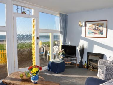 A living room with a glass door and windows overlooking the sea at Homestead in Aberdesach near Penygroes