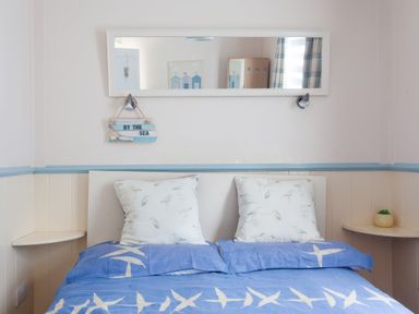 A bedroom with a double bed blue bedding white pillows wall mirror and small shelves at Homestead in Aberdesach near Penygroes