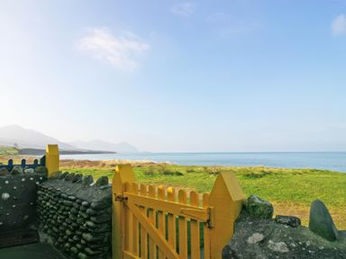 A yellow wooden gate with stone walls overlooking green grass and the sea at Homestead Aberdesach near Penygroes