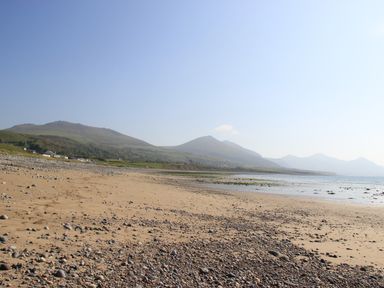 A sandy and rocky beach with mountains and houses in the background at Homestead in Aberdesach near Penygroes