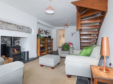 A living room with armchairs a fireplace a wooden staircase a bookshelf and a lamp at Quarrymans cottage in Beddgelert