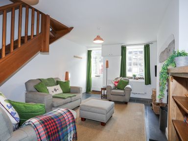 A living room with gray sofas green cushions and curtains under a wooden staircase at Quarrymans cottage in Beddgelert
