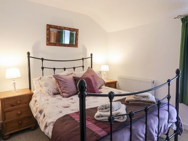 A bedroom with a bed with pillows and folded towels on it two wooden nightstands with lamps and a wall mirror at Quarrymans cottage in Beddgelert
