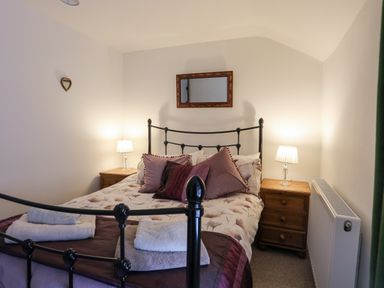 A bedroom with a black metal bedframe bedside tables with lamps and folded towels at Quarrymans cottage in Beddgelert