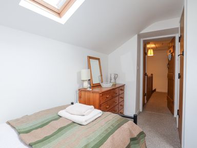 A bedroom with a bed covered with a striped blanket and folded towels on top a wooden dresser with a mirror lamp and pitcher a skylight window and wooden door at Quarrymans cottage in Beddgelert