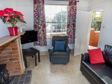 A living room with a blue armchair a black sofa with a red cushion a fireplace a small black table with a television and floral curtains at 1 Willow Cottage in Upton Upon Severn
