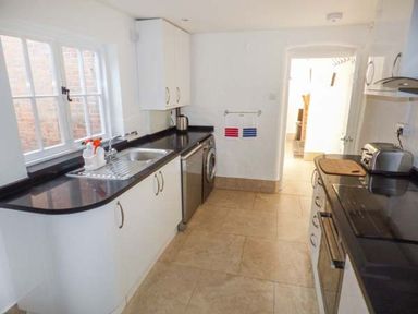 A kitchen with white cabinets black countertops a sink window and appliances at 1 Willow Cottage in Upton Upon Severn