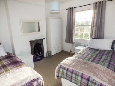 A bedroom with two single beds a window with curtains a wardrobe and a fireplace at 1 Willow Cottage in Upton Upon Severn