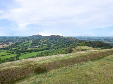 A grassy hill overlooking a patchwork of fields and forested hills in Upton Upon Severn