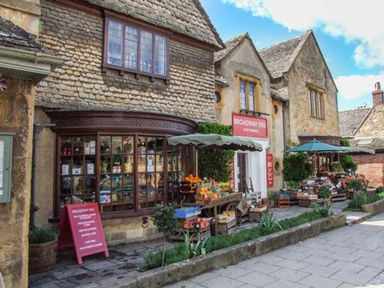 An outdoor market display with fruits and vegetables outside a stone building with a sign reading Broadway Deli at 1 Willow Cottage in Upton Upon Severn
