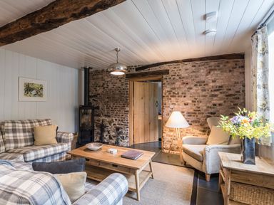 A living room with a plaid sofa and armchair a wooden coffee table and a wood burning stove at Tan Llan in Llanelltyd near Dolgellau