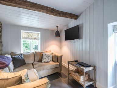A sitting area with a beige sofa a wall mounted TV a small table and a window at Tan Llan in Llanelltyd near Dolgellau