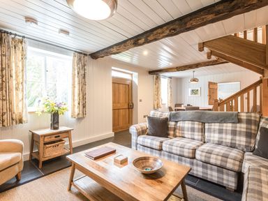 A living room with a plaid sofa wooden coffee table flowers on a side table and visible wooden stairs at Tan Llan in Llanelltyd near Dolgellau