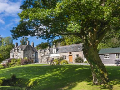 A large stone house with chimneys and windows surrounded by grass and trees at Tan Llan in Llanelltyd near Dolgellau