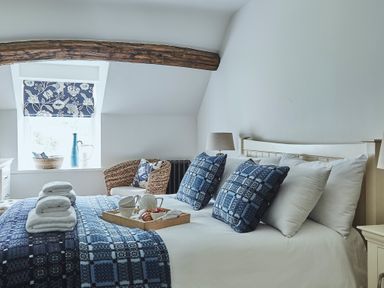 A bedroom with a bed featuring blue patterned pillows and blankets a wicker chair and a wooden beam at Tan Llan in Llanelltyd near Dolgellau