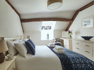 A bedroom with a bed folded towels and blue patterned bedding near wooden beams and white furniture at Tan Llan in Llanelltyd near Dolgellau