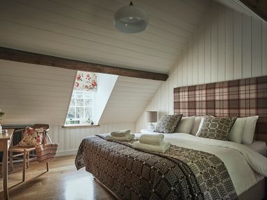 A bedroom with a large bed and patterned bedding under a slanted ceiling at Tan Llan in Llanelltyd near Dolgellau