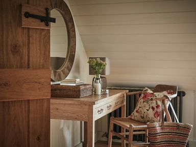 A wooden desk with a round mirror above it and a chair with a floral cushion next to a woven bag at Tan Llan in Llanelltyd near Dolgellau