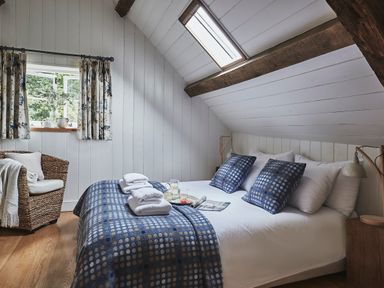 A bedroom with a double bed two blue patterned cushions stacked towels wicker chair and windows at Tan Llan Llanelltyd near Dolgellau