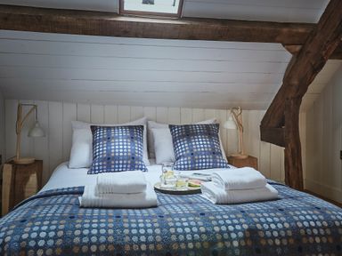 A bedroom with a bed covered in blue patterned bedding with folded white towels and wooden bedside tables with lamps at Tan Llan in Llanelltyd near Dolgellau