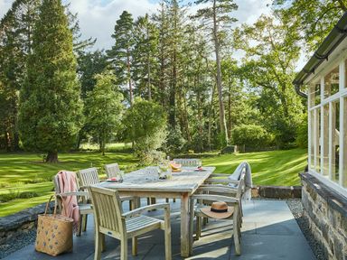 An outdoor wooden dining table with chairs on a patio next to a building surrounded by grass and trees at Tan Llan in Llanelltyd near Dolgellau