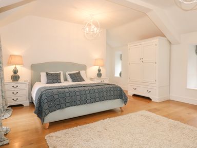 A bedroom with a double bed bedside tables with lamps a wardrobe and a rug on wooden floor at Tan Llan in Llanelltyd near Dolgellau
