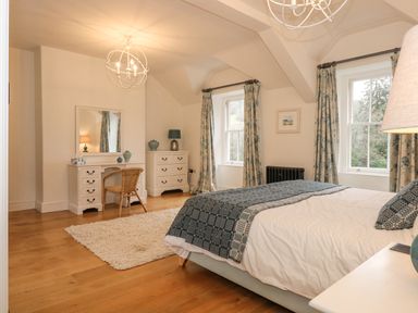 A bedroom with a bed a white dresser a mirror a chair and windows at Tan Llan in Llanelltyd near Dolgellau