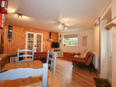 A living room with wooden dining table and chairs a leather sofa a TV on a stand and a wooden chest at The Aqua Shack in Newquay