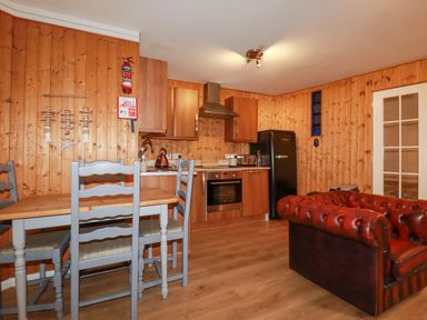 A kitchen and dining area with wooden walls a black fridge wooden cabinets a wooden table with gray chairs and a red leather sofa at The Aqua Shack in Newquay
