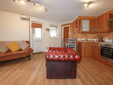 A kitchen and living area with a brown leather sofa a red leather chair wooden cabinets and a small dining table at The Aqua Shack in Newquay
