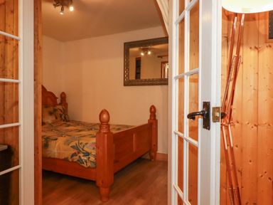 A bedroom with a wooden bed frame and patterned bedding next to a wall mirror at The Aqua Shack in Newquay