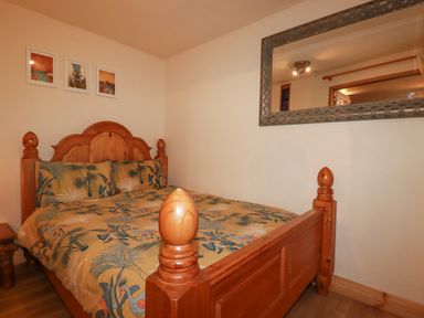 A bedroom with a wooden bed with patterned bedding a bedside table and framed pictures on the wall at The Aqua Shack in Newquay