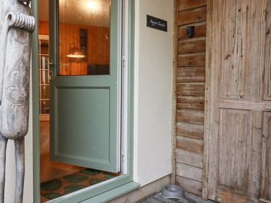 An open green door leading to a room with wooden walls and a lamp a carved wooden sculpture near the door a wooden door and a pet bowl on the floor at The Aqua Shack in Newquay
