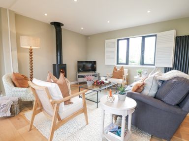 A living room with chairs a sofa a glass coffee table a floor lamp and a wood stove at Holm Oaks Cottage in Busbridge near Godalming