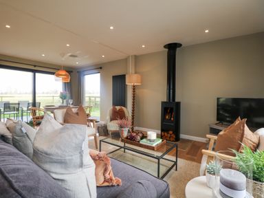 A living room with a modern wood stove glass coffee table and dining area with large windows at Holm Oaks Cottage in Busbridge near Godalming
