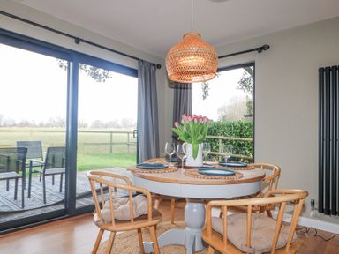 A dining area with a round table set with plates and glasses and wooden chairs with cushions at Holm Oaks Cottage in Busbridge near Godalming