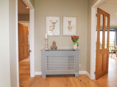A hallway with a radiator cover holding a candle holder statue and vase of flowers at Holm Oaks Cottage Busbridge near Godalming